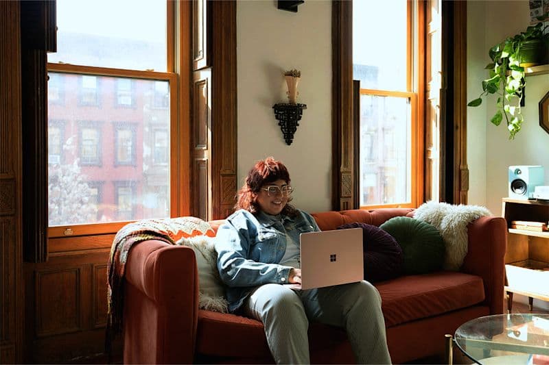 A woman sitting in a sofa smiling towards a computer